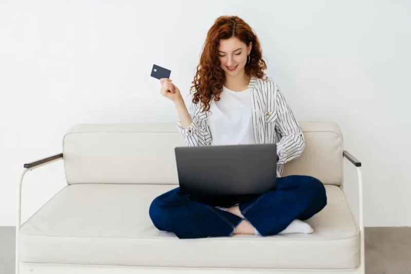 Femme sur le point de faire un achat, avec une carte bancaire et son ordinateur sur les genoux